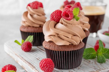 Kremalı çikolatalı kekler taze ahududu ve gri beton arka planda nane yapraklarıyla süslenmiş. Lezzetli bayram tatlısı.