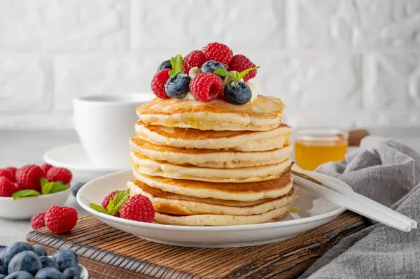 Krem şantili bir yığın krep, taze böğürtlen ve bal gri beton arka planda beyaz bir tabakta.