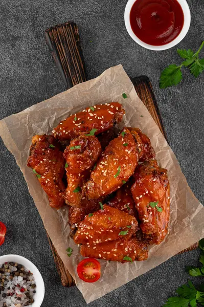 Acı biber soslu fırında tavuk kanadı ve koyu beton arka planda tahta bir tahtanın üzerinde susam tohumu. Üst görünüm, alanı kopyala