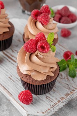 Kremalı çikolatalı kekler taze ahududu ve gri beton arka planda nane yapraklarıyla süslenmiş. Lezzetli bayram tatlısı.