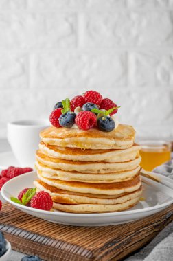 Krem şantili bir yığın krep, taze böğürtlen ve bal gri beton arka planda beyaz bir tabakta.