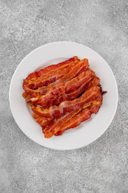 Kahvaltı için domuz pastırması, gri beton arka planda beyaz bir tabakta. Üst görünüm, alanı kopyala