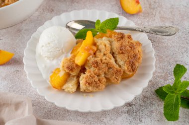 Ev yapımı şeftalili turta. Sulu şeftalili turta, bir kepçe vanilyalı dondurma ve beyaz tabakta taze nane. Rahatlatıcı yemek.