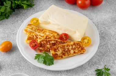 Kızarmış ve çiğ halloumi peyniri gri bir zeminde beyaz bir tabakta