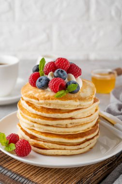 Krem şantili bir yığın krep, taze böğürtlen ve bal gri beton arka planda beyaz bir tabakta.
