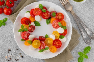 Kiraz domatesli Caprese salatası, mini mozzarella, pesto sosu ve beyaz tabakta taze fesleğen. Sağlıklı vejetaryen yemeği.