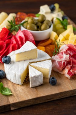 Çeşitli peynirli Charcuterie tahtası, salam, korizzo, prosciutto, bal, üzüm, fındık, zeytin, ekmek, yabanmersini ve koyu ahşap arka planda taze otlar. Şenlikli bir atıştırmalık