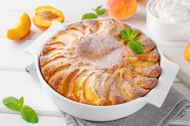 Beyaz ahşap zemin üzerinde beyaz seramik fırın şeklinde nefis şeftalili turta. Yaz pastası. Seçici odak, boşluğu kopyala