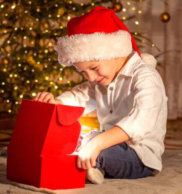 Noel Baba şapkalı bir çocuk hediye kutusunu açar ve gülümser. Noel, seçici odaklanma. Yüksek kalite fotoğraf