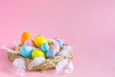 Fotokopi uzayı olan pembe arka planda tüyleri olan bir yuvada paskalya yumurtaları. Yüksek kalite fotoğraf