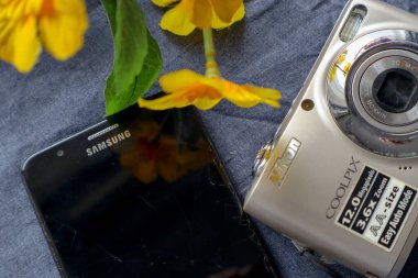 Bandung, Indonesia - June 1st 2024 : Old Nikon Coolpix L21 camera in silver cream color alongside a vintage Samsung smartphone with a cracked and dirty screen clipart