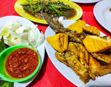 Pecel lele, kızarmış tavuk, tofu, tempeh, sambal pekel, taze sebze ve karıştırılmış su ıspanağı geleneksel Endonezya sokak yemeği menüsü..