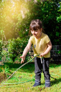 Küçük mutlu kız bahçe hortumuyla oynuyor. Anaokulu çocuğu bahçedeki ağaçları ve bitkileri sularken eğleniyor..