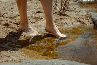 Side view of a woman's feet walking and feeling the cool water of a crystal clear river. Concept of healthy outdoor life.