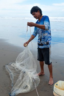 Central American fisherman preparing net on tropical beach.