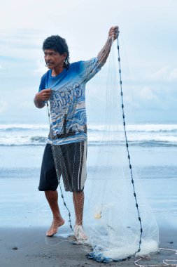 Central American fisherman preparing net on tropical beach.