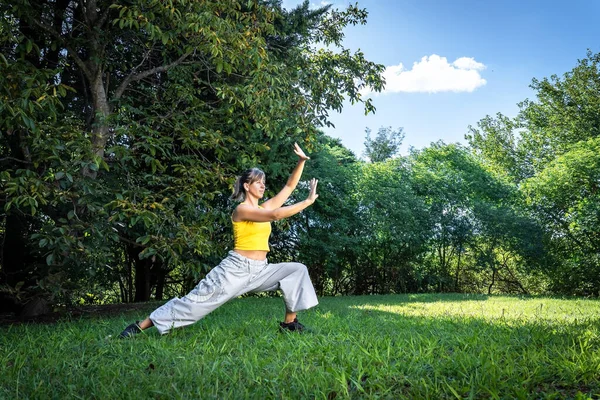 Serene adult woman doing qigong exercise in the park. Connection to nature and the vital energy of the universe.