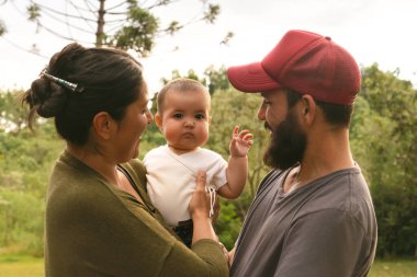 Mutlu aile, baba ve anne gülümseyen ve küçük kıza bakan küçük kız yeşil çayır arka planındaki kameraya merakla bakıyor. Dışarıdaki insanları kapatın..