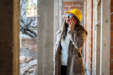 Sarı kasklı başarılı kadın müteahhit portresi cep telefonuyla arama yapıyor. Kadın mimarın portresi. Yapıma bakıyor ve cep telefonunda fotokopi alanı ile konuşuyor..
