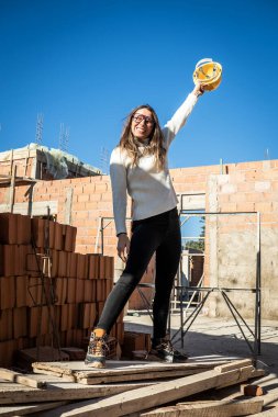Başarılı bir kadın mühendis. Kadın mimarın dikey portresi. İnşaat alanında gülümseyen ve sarı şapkasıyla kameraya bakan..