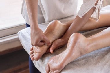 Genç bir kadın refleksoloji tedavisi görüyor. Terapistin ellerine yakın çekim yaparak hastanın ayaklarına masaj yapıyor..