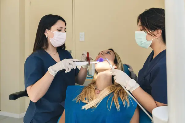 Young woman during teeth whitening procedure with curing UV light at dentist\'s office