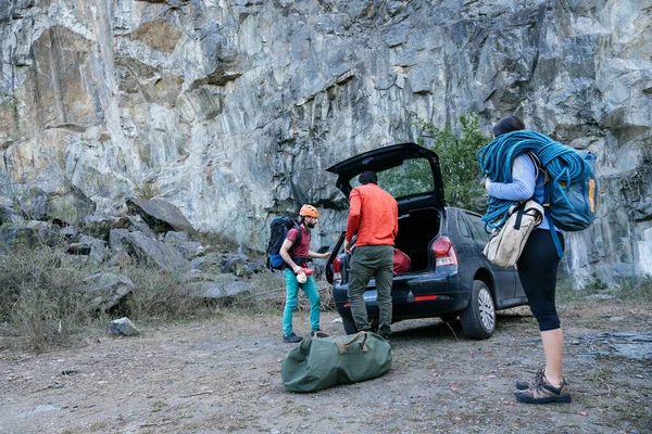 Group of young people at the foot of the mountain unloading rock climbing gear. Concept of friendship, extreme sport and teamwork.
