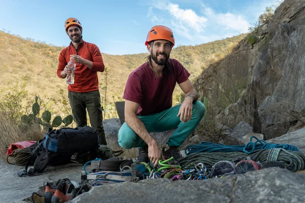 Smiling men preparing climbing gear. A bundle of rock climbing equipment.