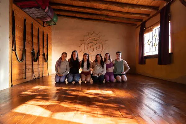 Group portrait of a community of people practicing yoga smiling and looking at the camera. General shot illuminated with natural light coming in through side windows.