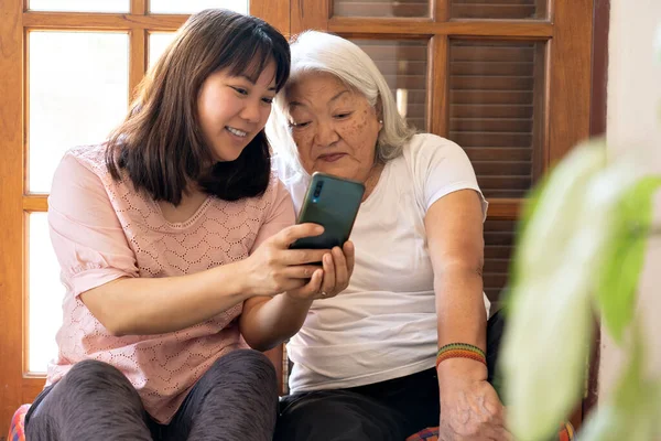 Japanese adult daughter shares photos taken with her smartphone with her elderly mother.