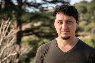 Orta yaşlı beyaz bir adamın yakından çekilmiş portresi. Bakışları ve açık havada hafif bir gülümsemesi var..