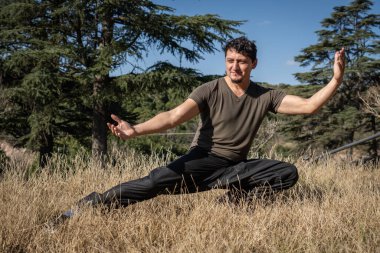 Yetişkin bir adam, fiziksel ve zihinsel eğitimine odaklanmış, doğal bir parkta Kung Fu yapar.