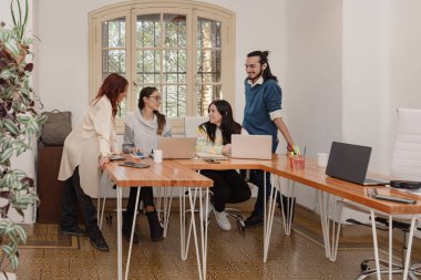 Çeşitli girişimcilerden oluşan bir grup, parlak bir ofiste coşku ve motivasyonla ortak bir proje üzerinde çalışmaktadır..