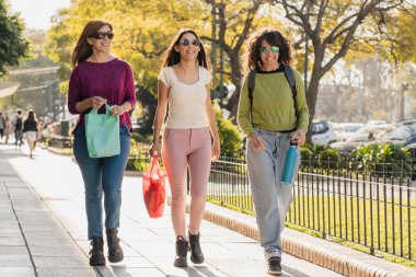 Güneşli bir günde, dışarıda mutlu mesut dolaşan, alışveriş torbaları taşıyan, günlük kıyafetler ve güneş gözlüğü takan, birlikte vakit geçirmenin keyfini çıkaran üç kadından oluşan bir grup..