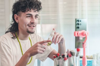 Sosyal medya takipçileri için video kaydederken güzellik serumu şişesi gösteren genç bir erkek içerik yaratıcısı, kozmetik markasını tanıtıyor ve makyaj ipuçlarını paylaşıyor