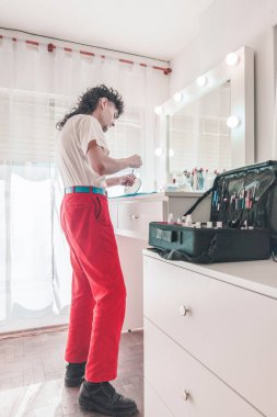 Genç erkek makyaj sanatçısı canlı bir güzellik salonunda fırça ve kozmetik hazırlıyor, çeşitlilik ve kapsamı kutluyor ve modern güzellik standartlarının özünü somutlaştırıyor.