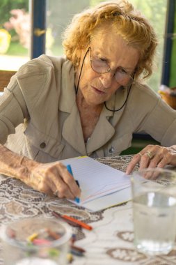 Bir bardak suyla bir masada elinde boya kalemleriyle resim çizen yaşlı bir kadın emekliliğinde rahatlatıcı ve yaratıcı bir aktivitenin tadını çıkarıyor.