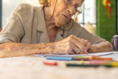 Evde sanat terapisinden hoşlanan, renkli boya kalemleriyle çizen, boş zamanlarında sanatsal uğraşları sayesinde rahatlayan ve yaratıcı ifadeleri benimseyen yaşlı bir kadın.