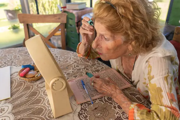 Üst düzey bir kadın masada otururken makyaj yapıyor, çapraz bulmaca üzerinde çalışıyor ve boş zamanlarının tadını çıkarıyor, aktif bir yaşam tarzını benimsiyor ve rahatlama anlarından zevk alıyor.