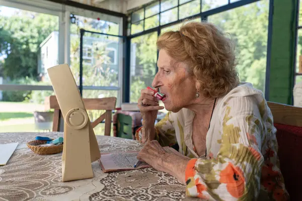 Kıdemli kadın rahat evinde bir masada oturuyor, küçük bir aynayla kırmızı ruj sürüyor, güzellik rutinini kucaklıyor ve kendinden emin bir şekilde önümüzdeki güne hazırlanıyor.