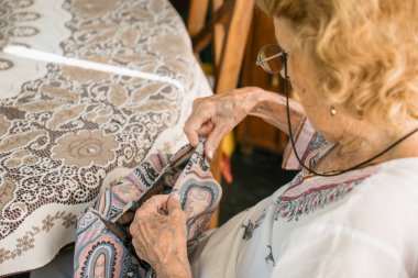 Kıdemli terzi kumaşı dikkatlice dikiyor, uzmanlık gösteriyor ve terzilik üzerine odaklanıyor, elleriyle iğne ve ipliği ustaca manipüle ediyor, tekstil üzerinde karmaşık desenler yaratıyor.