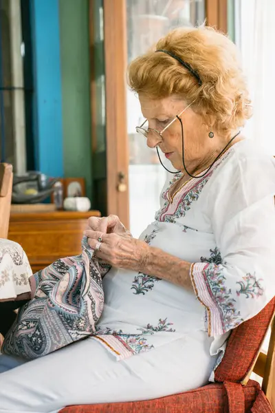 Üst düzey kadın gözlük takıyor, evinde rahat bir şekilde otururken desenli kumaş dikmeye odaklanıyor emekliliği sırasında rahatlatıcı bir hobisinin keyfini çıkarıyor.