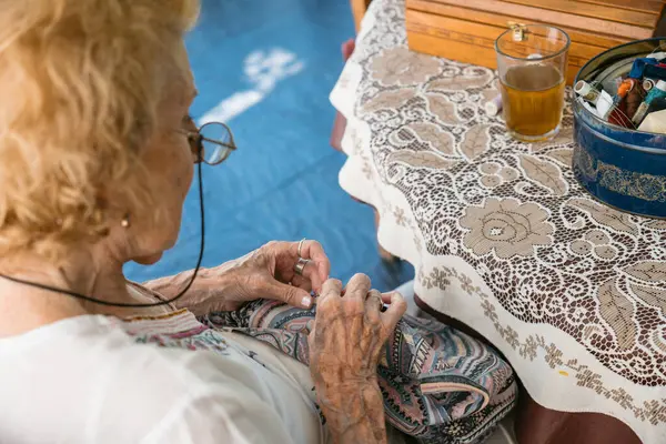 Üst düzey bir kadın hobisinden zevk alıyor, evinde renkli bir kumaş parçası dikiyor, bir bardak çay ve ince bir dantel masa örtüsüyle kaplı bir masaya dikiş setiyle.