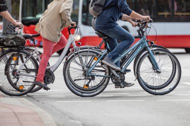 Arka planda bir otobüs sürerken birkaç bisikletçi caddeyi geçiyor.
