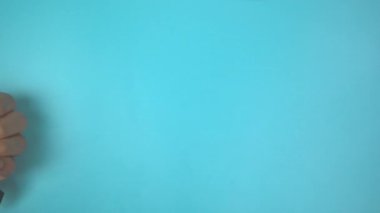 Görüntü 4K. Mavi arka planda deniz mavisi kurdelesini tutan eller... Yumurtalık Kanseri Bilinci, Jinekoloji, Rahim Kanseri, Vulvar Kanseri, Panik Bozukluğu, Travma Sonrası Stres Bozukluğu (PTSD)).