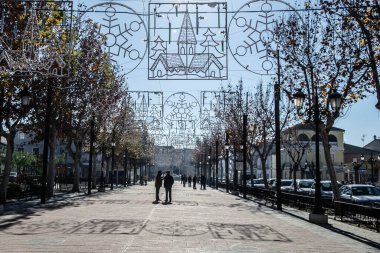 Kenarlarında ağaçlar, insan siluetleri ve Noel süsleri olan bir sokak geçidi.