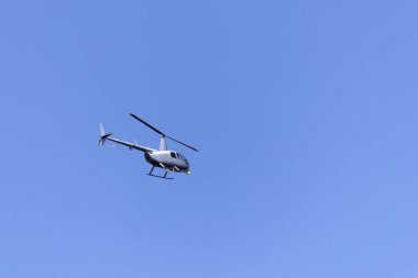 Gri bir helikopter bulutlarla mavi gökyüzünü geçiyor. Ulaşım. Kentsel.