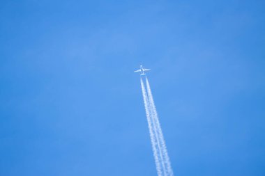 Mavi gökyüzünü geçen bir uçak arkasında beyaz bir buhar bırakıyor..