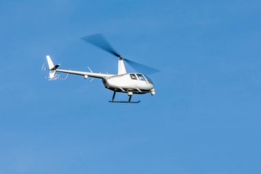 Gri bir helikopter bulutlarla mavi gökyüzünü geçiyor. Ulaşım. Kentsel.