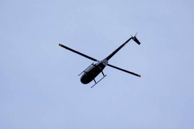 Siyah bir helikopter bulutlarla mavi gökyüzünü geçiyor. Ulaşım. Kentsel.